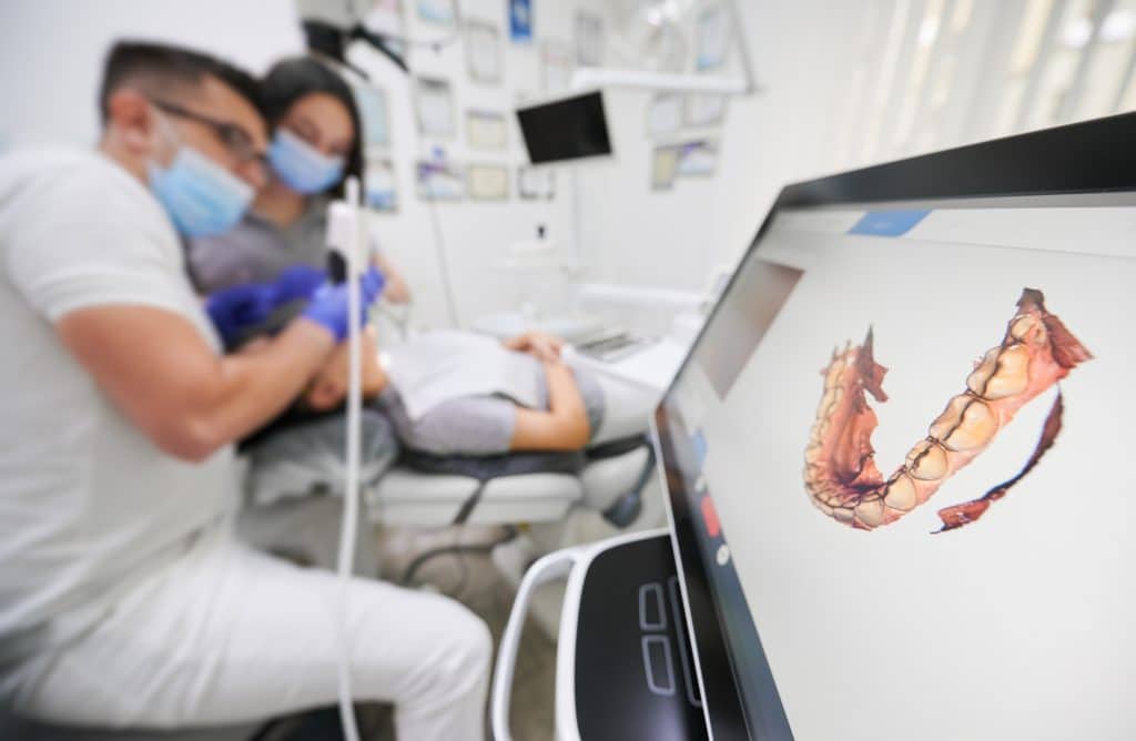 Dentist scanning patient's teeth with modern scanning machine. Digital print of patient's teeth is on big screen. Modern high precision technologies.