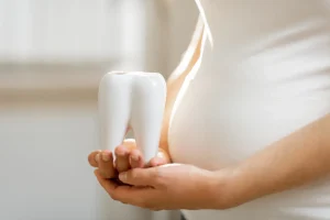 Pregnant woman holding a plastic model of a tooth.