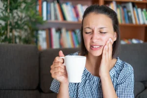 Young woman feeling tooth sensitivity while drinking hot coffee