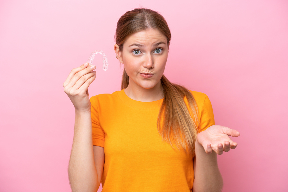 A girl holding a clear orthodontic aligner up to the camera