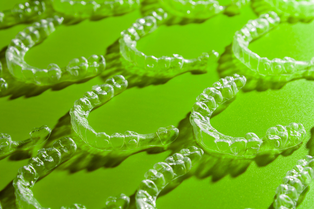 Clear aligners arranged on a green surface in a close-up shot.