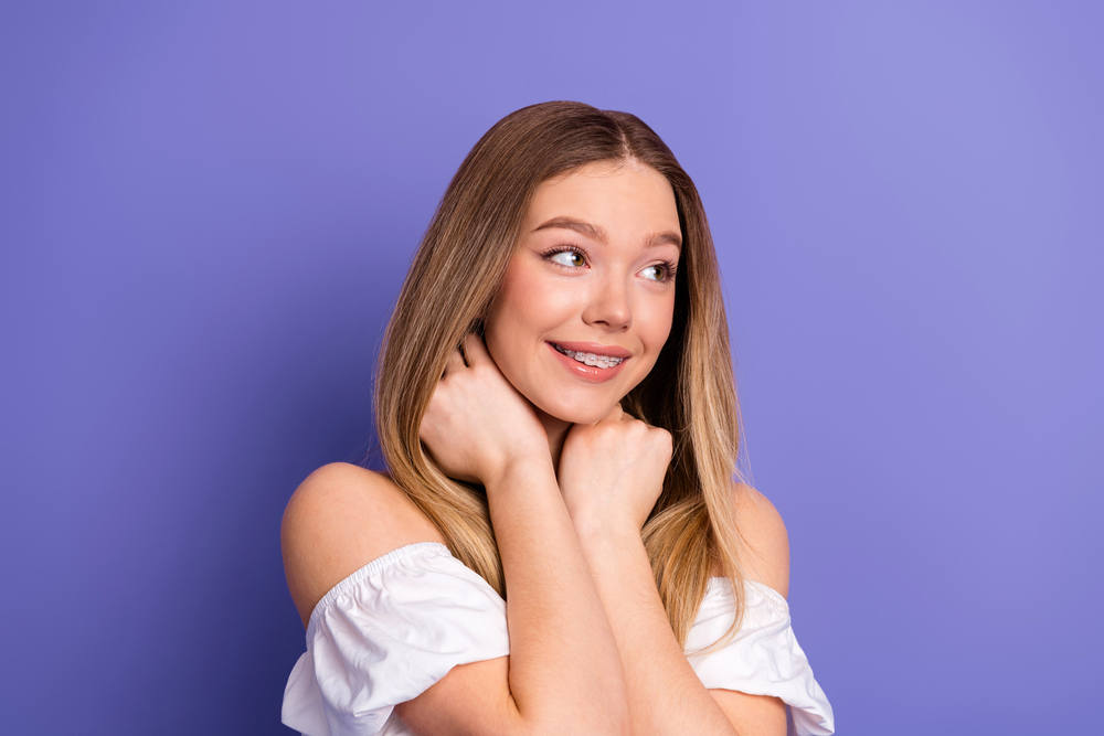 Smiling girl with fixed braces on a purple background.